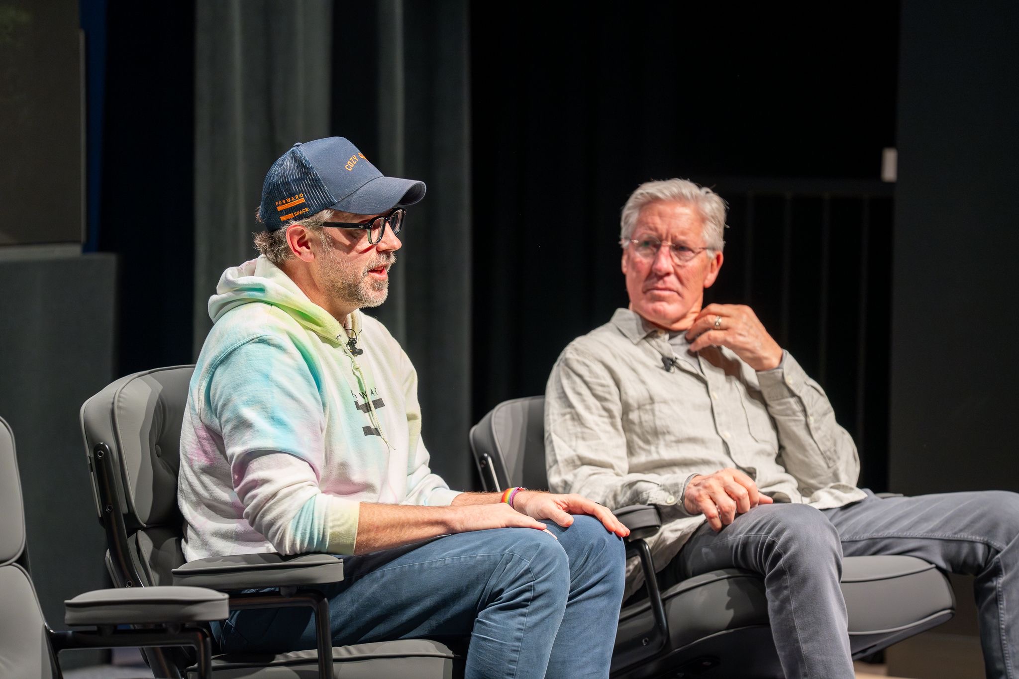 Sudeikis speaking while Carroll listens intently on stage